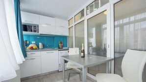 Een moderne keuken met witte kasten, een blauwe achterwand en een eethoek met een tafel en stoelen.