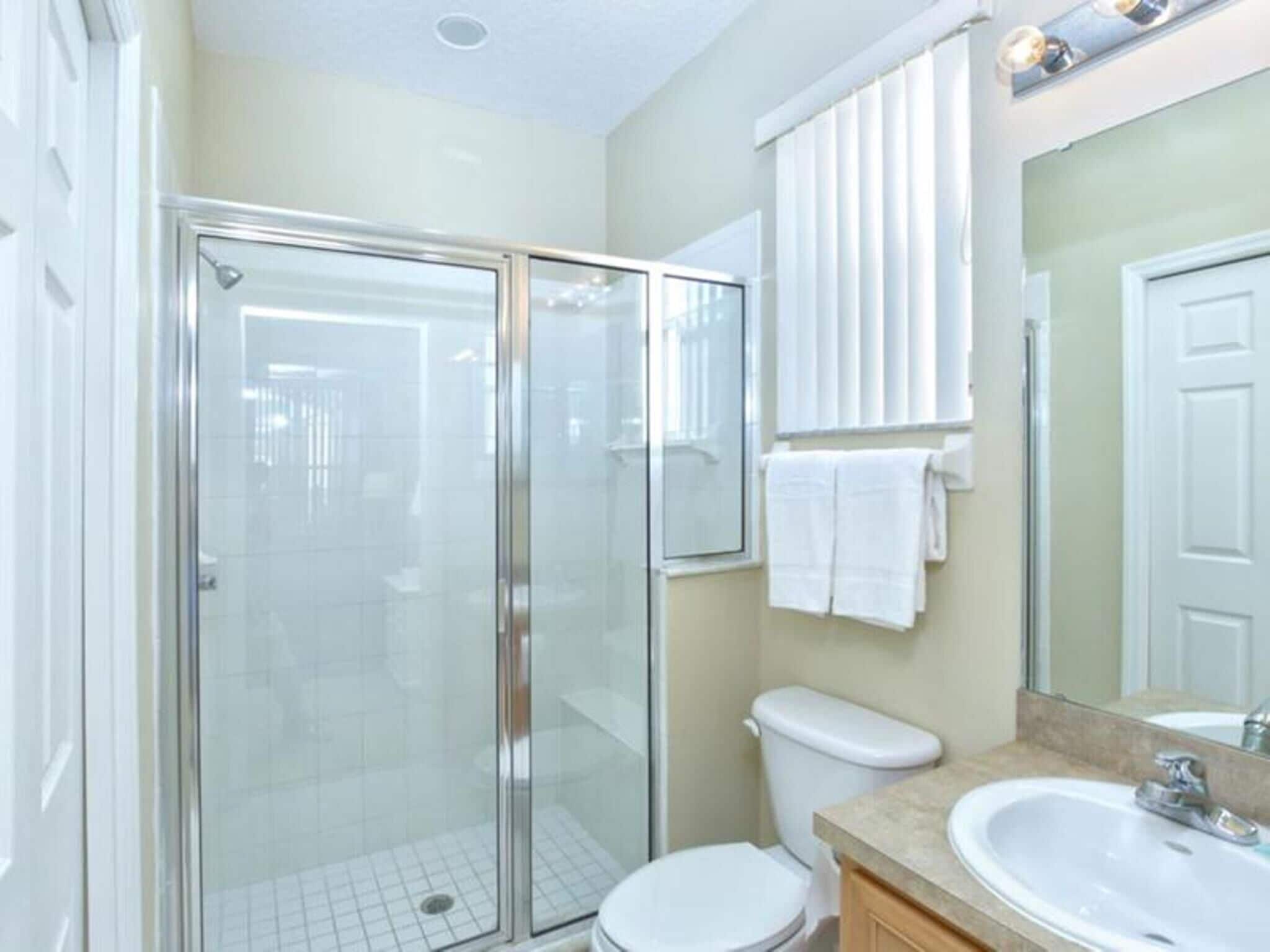 A modern bathroom with a glass-enclosed shower, a white toilet, and a sink with a mirror above it.