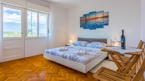 A bedroom with a bed, a nightstand, a table with a bottle of wine, and a chair.
