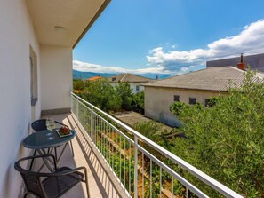Un balcon avec une table et des chaises, donnant sur un jardin et les bâtiments voisins.