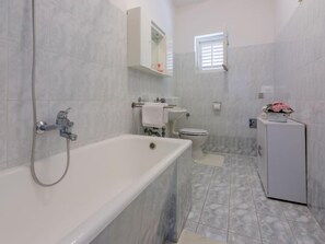 Une salle de bain avec une baignoire, des toilettes, un lavabo et un petit meuble orné d’une fleur.