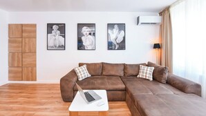 A living room with a brown leather sofa, a white coffee table with a laptop, and three framed pictures on the wall.