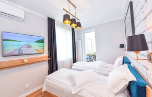 Habitación de hotel con dos camas, un televisor en la pared, una ventana con cortinas y una lámpara en la mesita de noche.