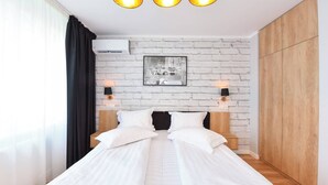 A neatly made bed with white linens and two pillows, a brick-patterned wall with a framed picture, and a wooden wardrobe.