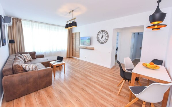Una sala de estar moderna con un sofá, una mesa de comedor con sillas, un televisor y un reloj en la pared.