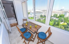 Una habitación con una mesa de madera y cuatro sillas, una cama, y un ventanal con vista a la ciudad.