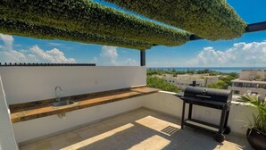 Eine Dachterrasse mit eingebautem Spülbecken, einem Grill und Blick auf die Stadtlandschaft.