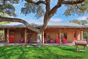 A log cabin with a porch, red chairs, and a mailbox. - Resort Suite Across the Street from Market Days - Sleeps 4! (Wimberley)