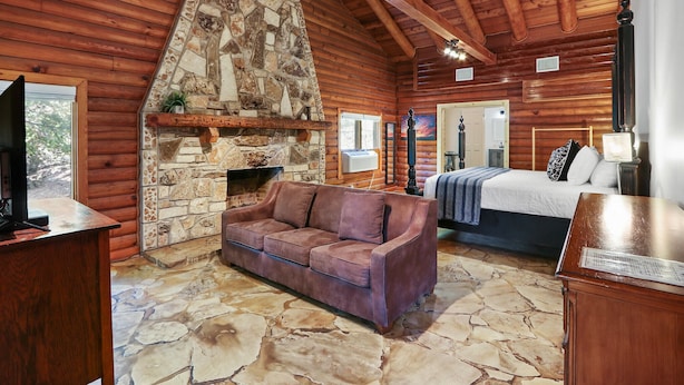 A log cabin interior with a stone fireplace, a sofa, a bed, and a wooden ceiling. - Resort Suite Across the Street from Market Days - Sleeps 4! (Wimberley)