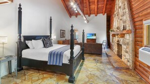 A bedroom with a four-poster bed, stone flooring, wooden ceiling beams, and a stone fireplace. - Resort Suite Across the Street from Market Days - Sleeps 4! (Wimberley)