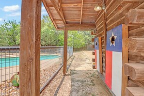 A wooden cabin with a covered porch, a pool, and a fenced area with trees in the background. - Resort Suite Across the Street from Market Days - Sleeps 4! (Wimberley)