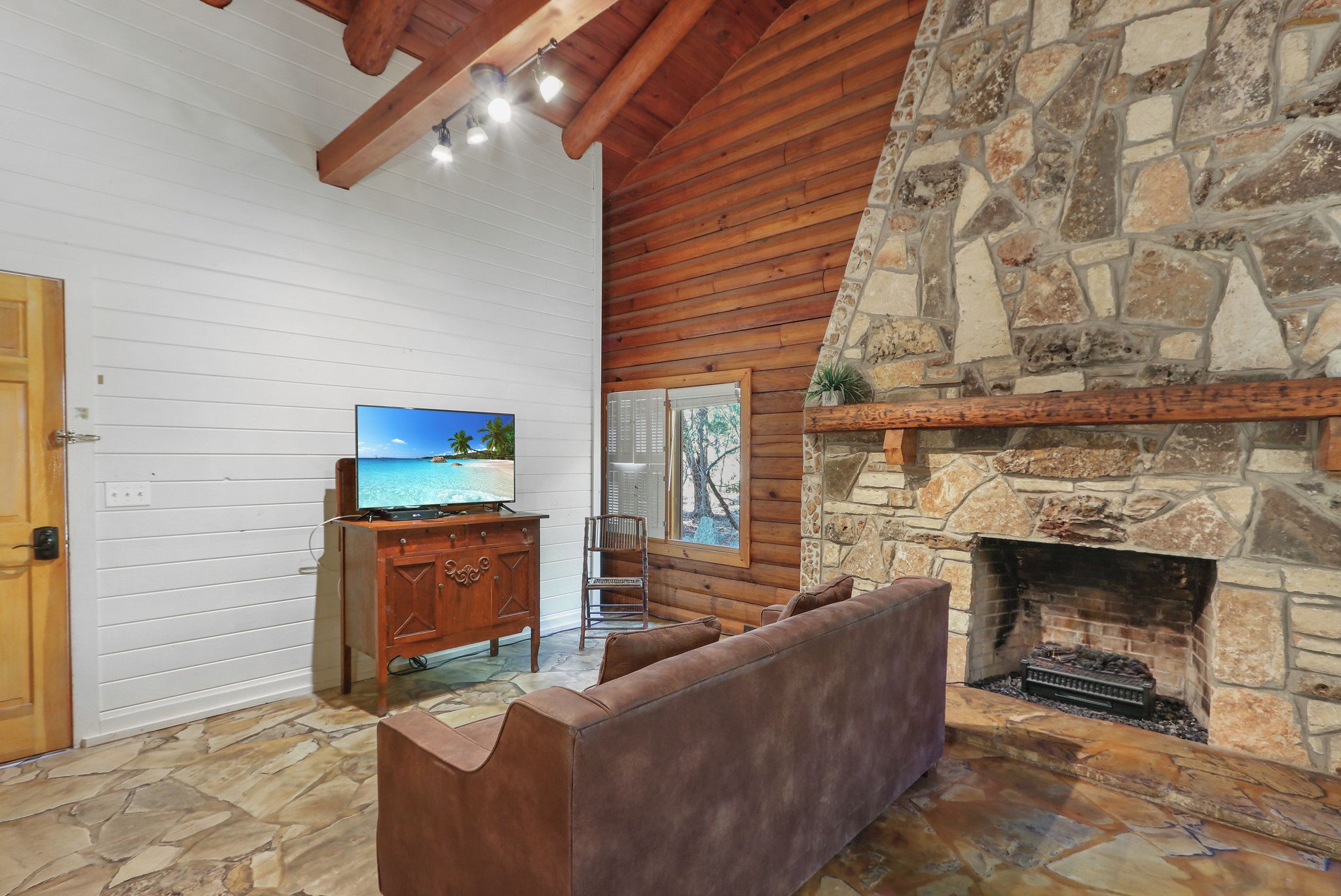 Una sala de estar acogedora con chimenea de piedra, vigas de madera, televisor y suelo de piedra.