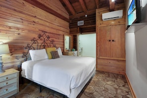 A wooden cabin bedroom with a bed, nightstands, a wardrobe, and a television. - King Bed with Resort Pool and Firepit! Minutes from Downtown (Wimberley)