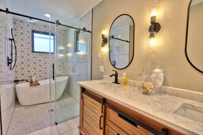 Un baño moderno con ducha envuelta en vidrio, una bañera independiente y un tocador con encimera de mármol.