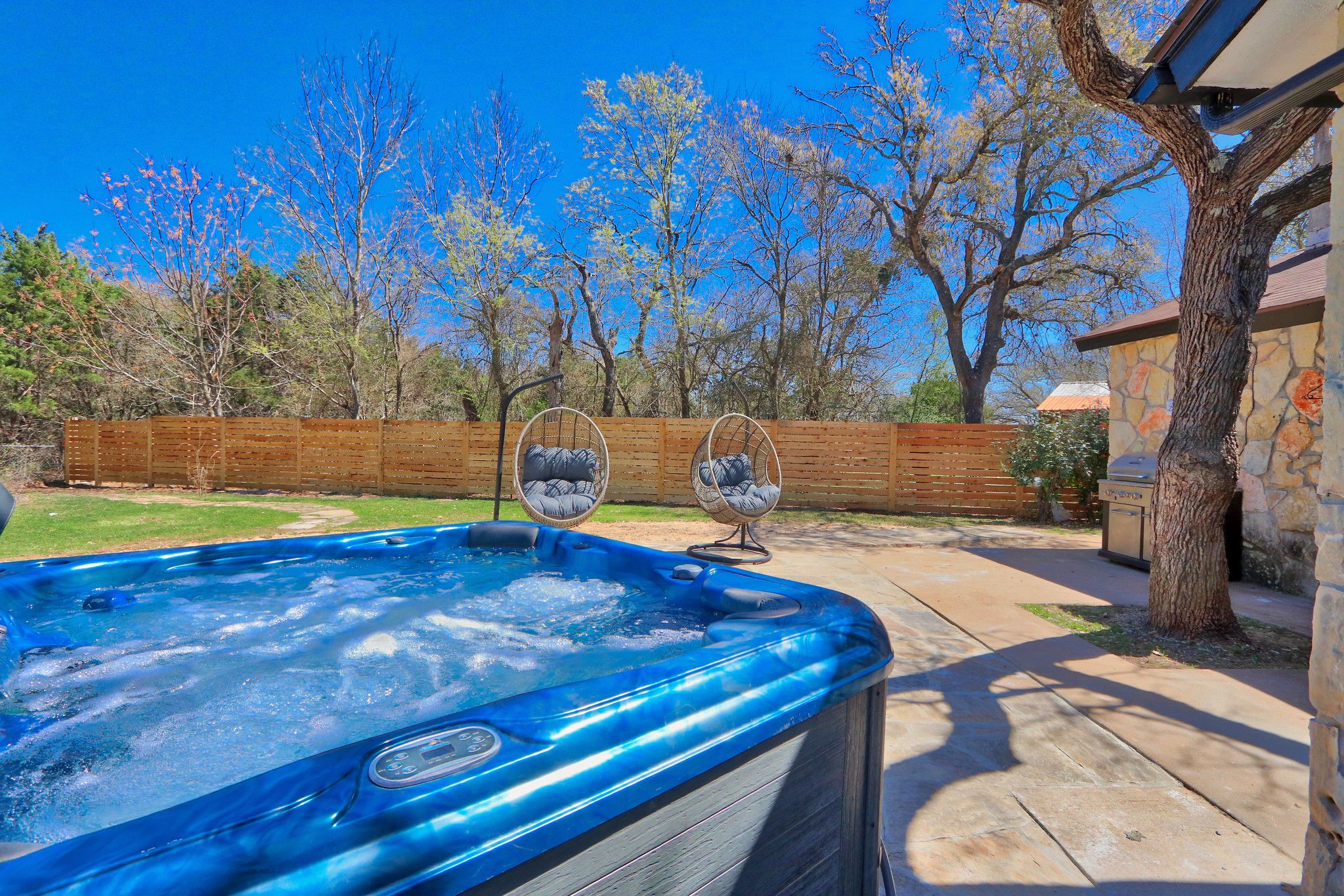 Un jacuzzi en un patio trasero con una cerca de madera, dos sillas y un edificio de piedra.