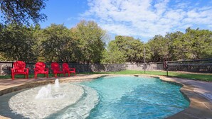 A swimming pool with a fountain, surrounded by red chairs and a stone deck. - King Bed with Resort Pool and Firepit! Minutes from Downtown (Wimberley)