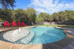 A swimming pool with a fountain, surrounded by red chairs and a stone deck.