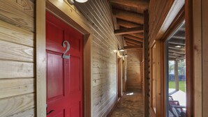 A wooden interior hallway with a red door, stone flooring, and a view of an outdoor deck. - King Bed with Resort Pool and Firepit! Minutes from Downtown (Wimberley)
