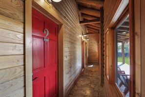 A wooden interior hallway with a red door, stone flooring, and a view of an outdoor deck.