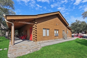 Een houten hut met een overdekte veranda, een pad van stenen en rode stoelen.