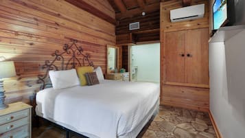 A wooden cabin bedroom with a bed, nightstands, a wardrobe, and a television.