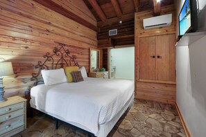 A wooden cabin bedroom with a bed, nightstands, a wardrobe, and a television.