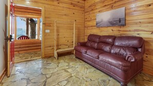 A wooden cabin interior with a stone floor, a leather sofa, a wooden ladder, and a painting on the wall. - King Bed with Resort Pool and Firepit! Minutes from Downtown (Wimberley)