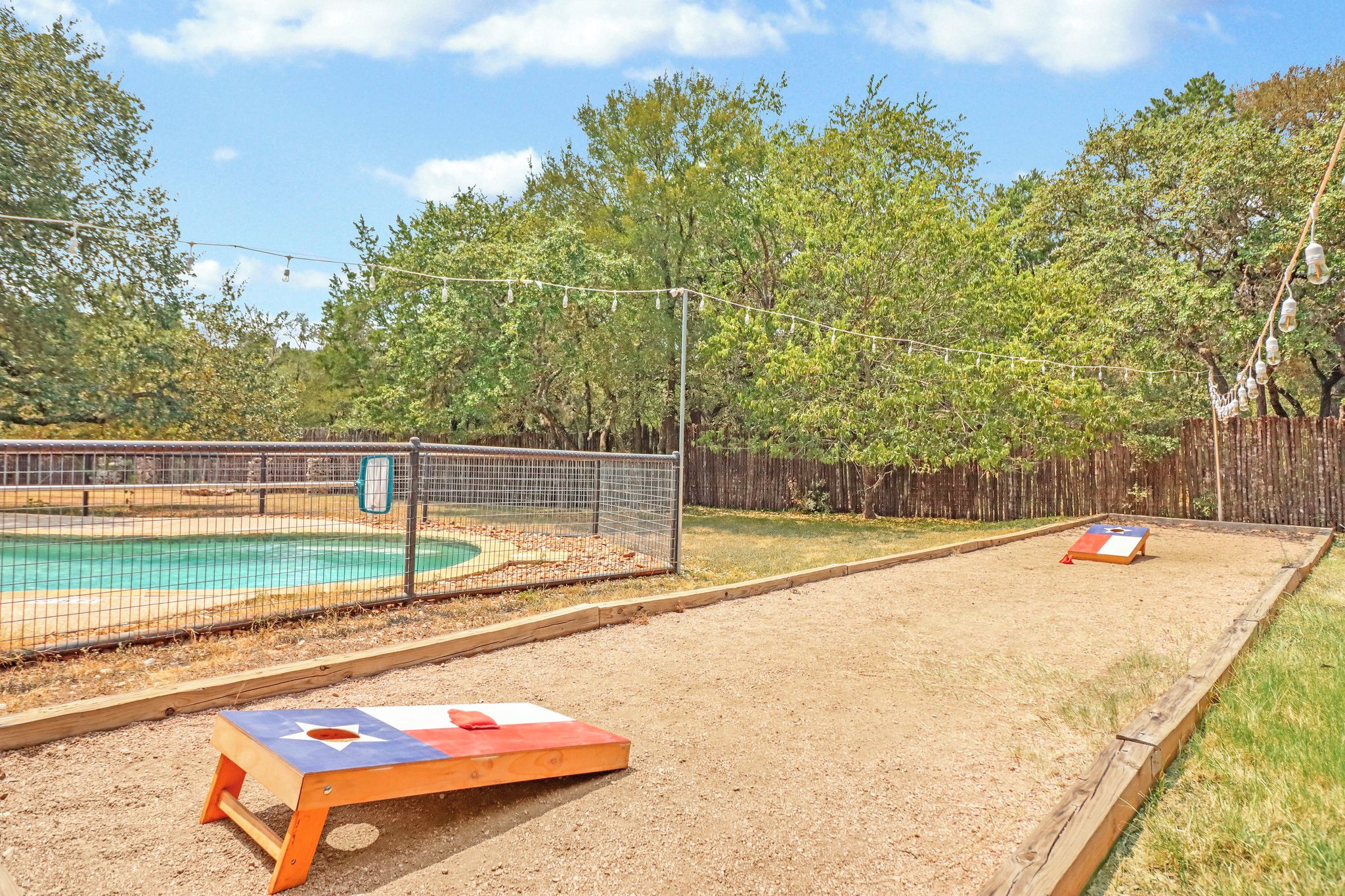 A fenced outdoor area with a pool, a wooden deck, and a sandy play area.