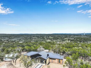 Ett modernt hus med ett tak av metall, omgivet av tät vegetation och en klar himmel.