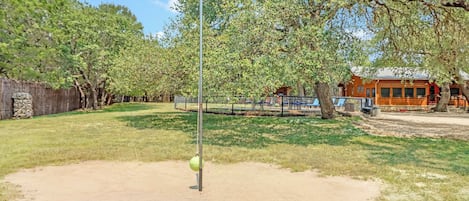 A fenced outdoor area with a sandpit, trees, and a building in the background.