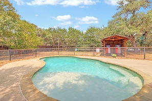 Una piscina cristalina con una estructura de madera cerca, rodeada por una valla y árboles.