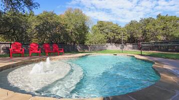 Una piscina con una fuente, rodeada de sillas rojas y una terraza de piedra.