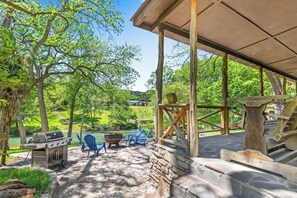 An outdoor patio with a grill, chairs, and a stone table. - The Guadalupe River right in your backyard! River living at its best! (Wimberley)