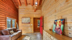 A log cabin interior with a stone floor, wooden walls, a brown leather sofa, a wooden dresser, and a painting of a cow. - WLCRS - Unit 4 -Walk to Market Days -  Resort Pool! (Wimberley)