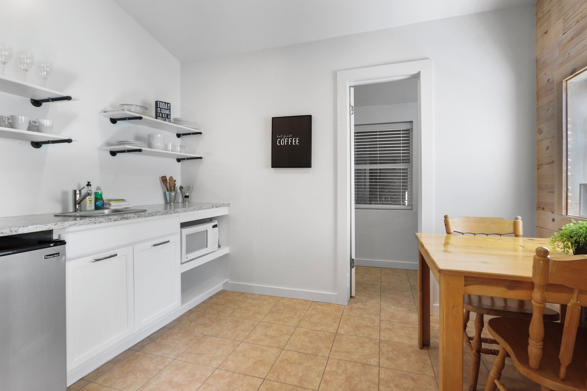 Una cocina moderna con armarios blancos, una mesa de comedor de madera y un letrero negro en la pared.