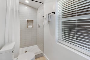 A bathroom with a toilet, shower, and window with blinds. - WLCRS - Unit 4 -Walk to Market Days -  Resort Pool! (Wimberley)