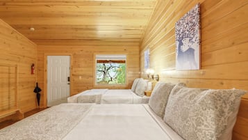 Una habitación de cabaña de madera con dos camas, una ventana con vista a árboles, un extintor y una lámpara fijada a la pared.