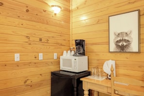 Une petite cuisine équipée d’un four à micro-ondes, d’une machine à café et d’un tableau représentant un raton laveur accroché au mur.