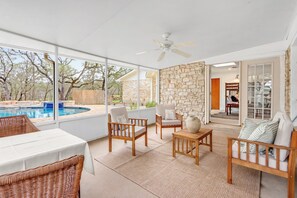Un patio con piscina, mobiliario de mimbre, muros de piedra y un ventilador de techo.