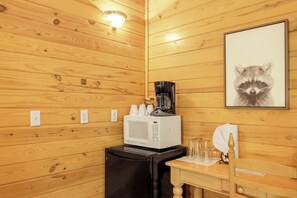 Une petite cuisine équipée d’un four à micro-ondes, d’une machine à café et d’un tableau représentant un raton laveur accroché au mur.