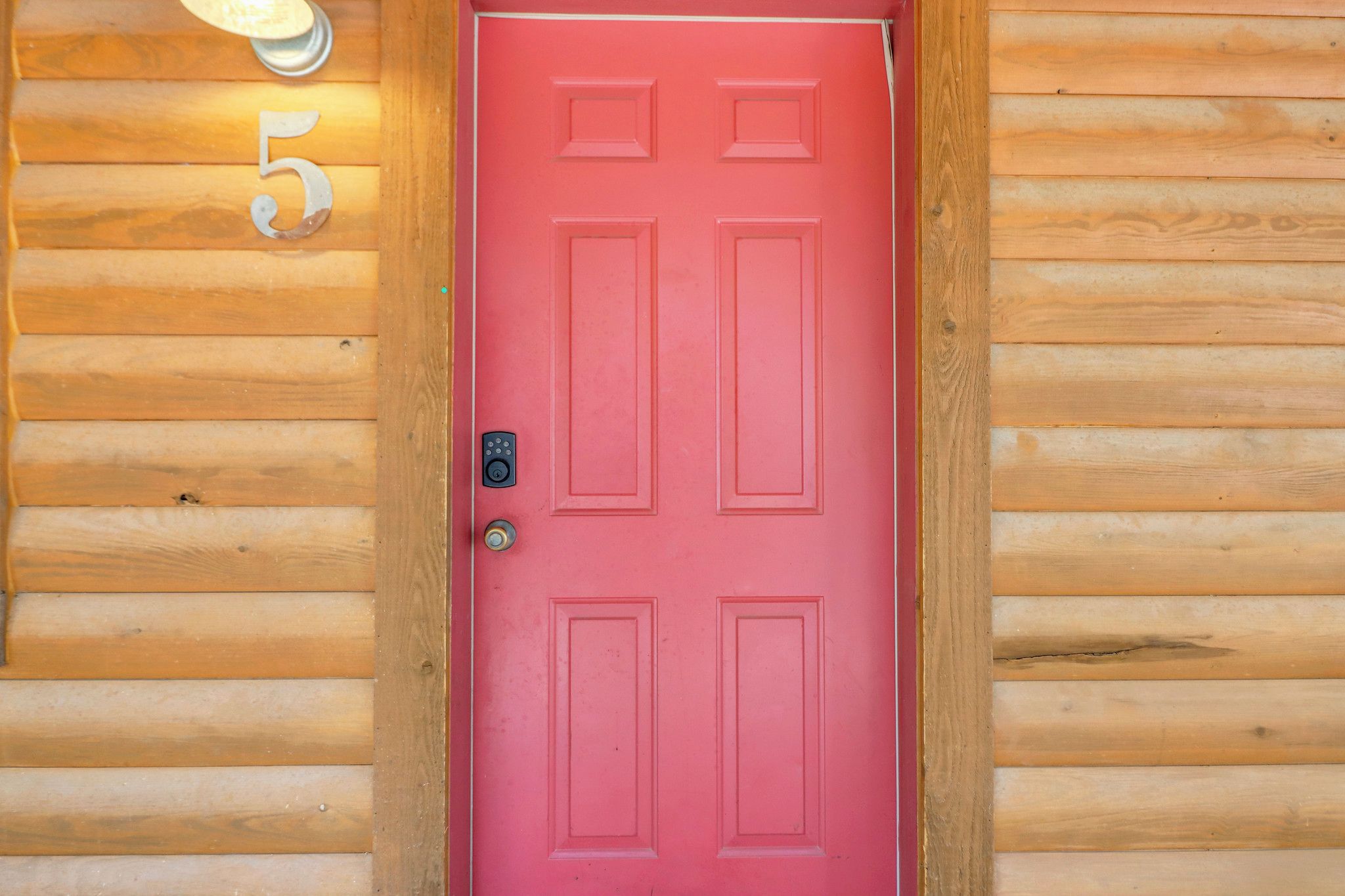 A red door with a keypad lock, set in a wooden log cabin with a number '5' sign above it.