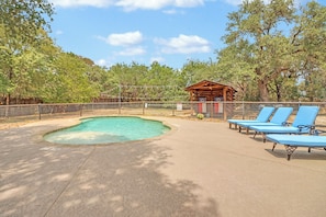 A pool area with a wooden cabin, lounge chairs, and a fenced enclosure. - Hotel Style Suite with Two Queen Beds - Minutes from Downtown! (Wimberley)