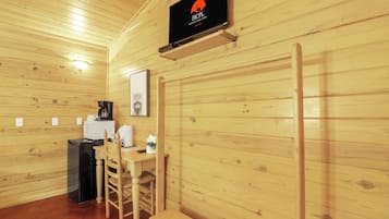 Un interior de madera con un letrero colgado, una mesa con sillas, una cafetera y un cesto de basura.