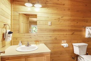 A wooden cabin bathroom with a sink, mirror, and toilet. - Hotel Style Suite with Two Queen Beds - Minutes from Downtown! (Wimberley)