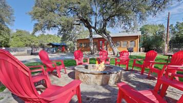 A fire pit surrounded by red chairs in an outdoor setting with a wooden building in the background.