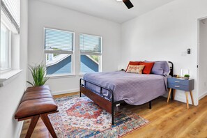 Une chambre à coucher avec un lit, une table de chevet, une commode et une fenêtre avec des stores.