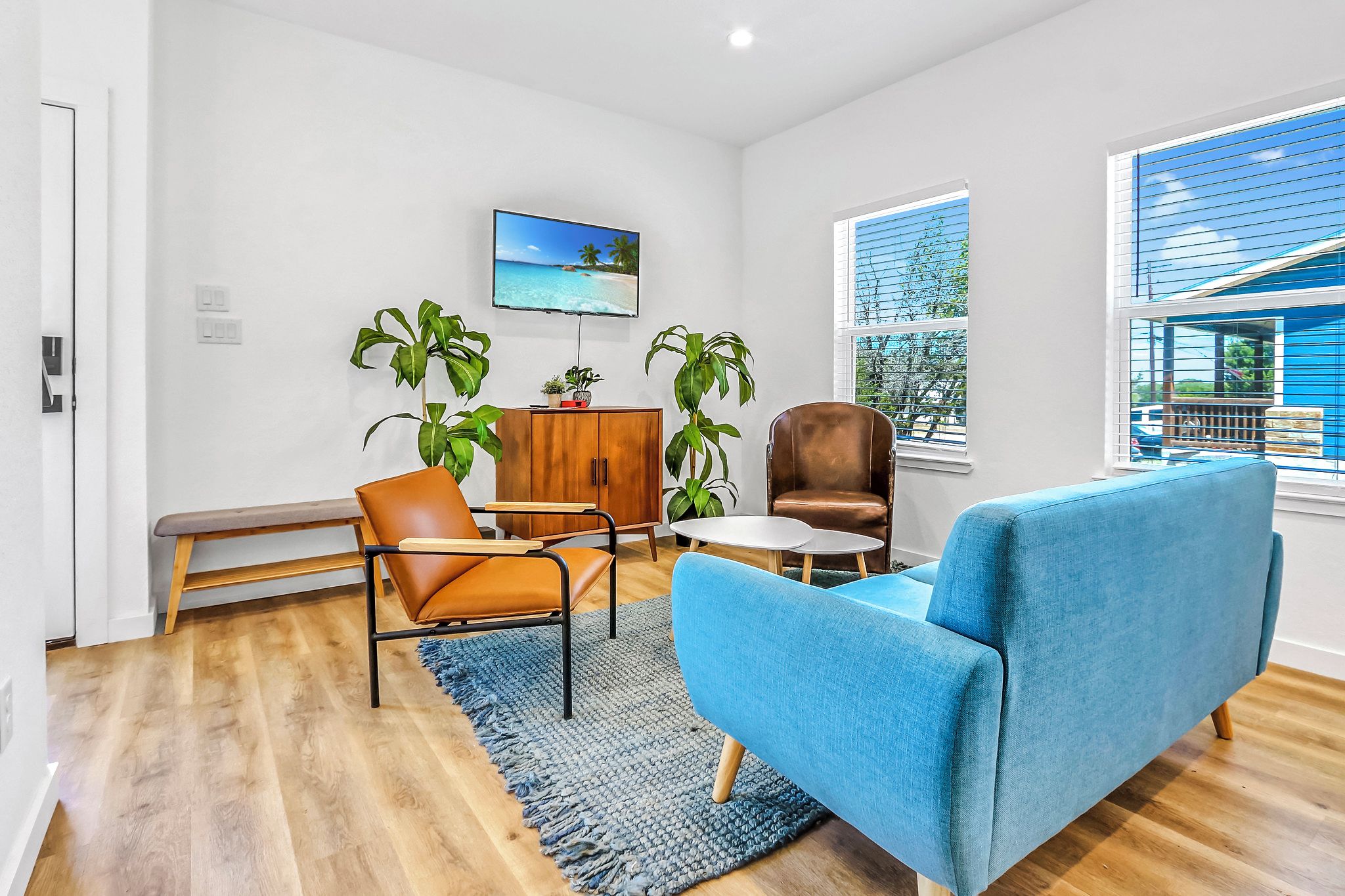 A modern living room with a blue sofa, brown leather chairs, a wooden cabinet, and a TV displaying a beach scene.