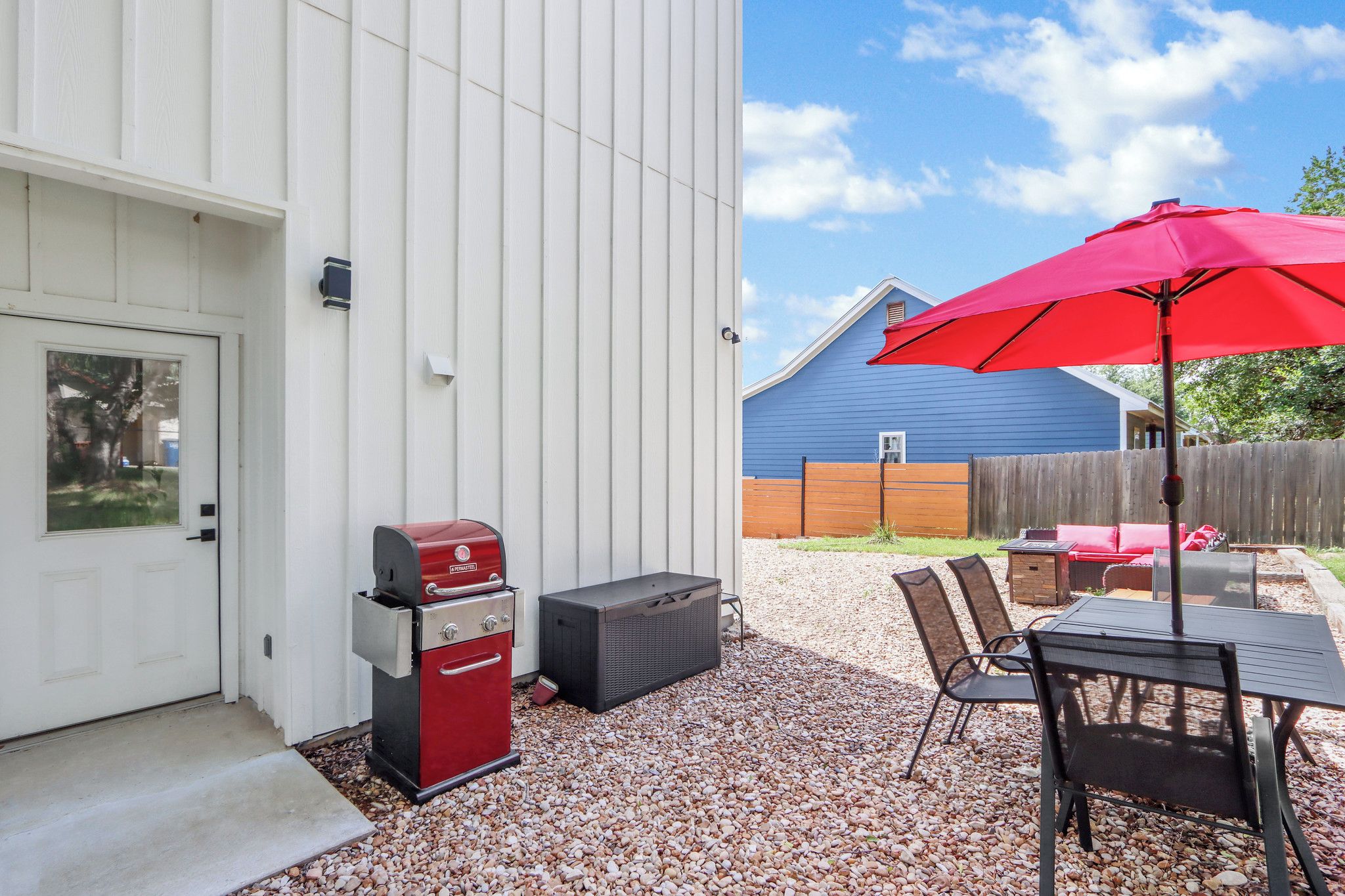 A backyard with a barbecue grill, a table with chairs, and a red umbrella.