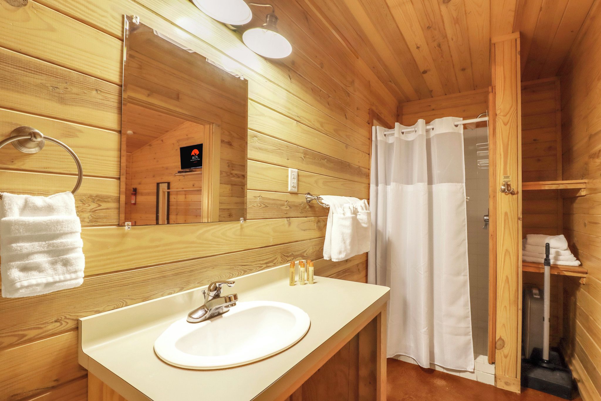 Ein Badezimmer in einer Holzhütte mit Waschbecken, Spiegel, Handtuchhalter und Duschvorhang.