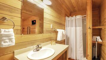 Ein Badezimmer in einer Holzhütte mit Waschbecken, Spiegel, Handtuchhalter und Duschvorhang.